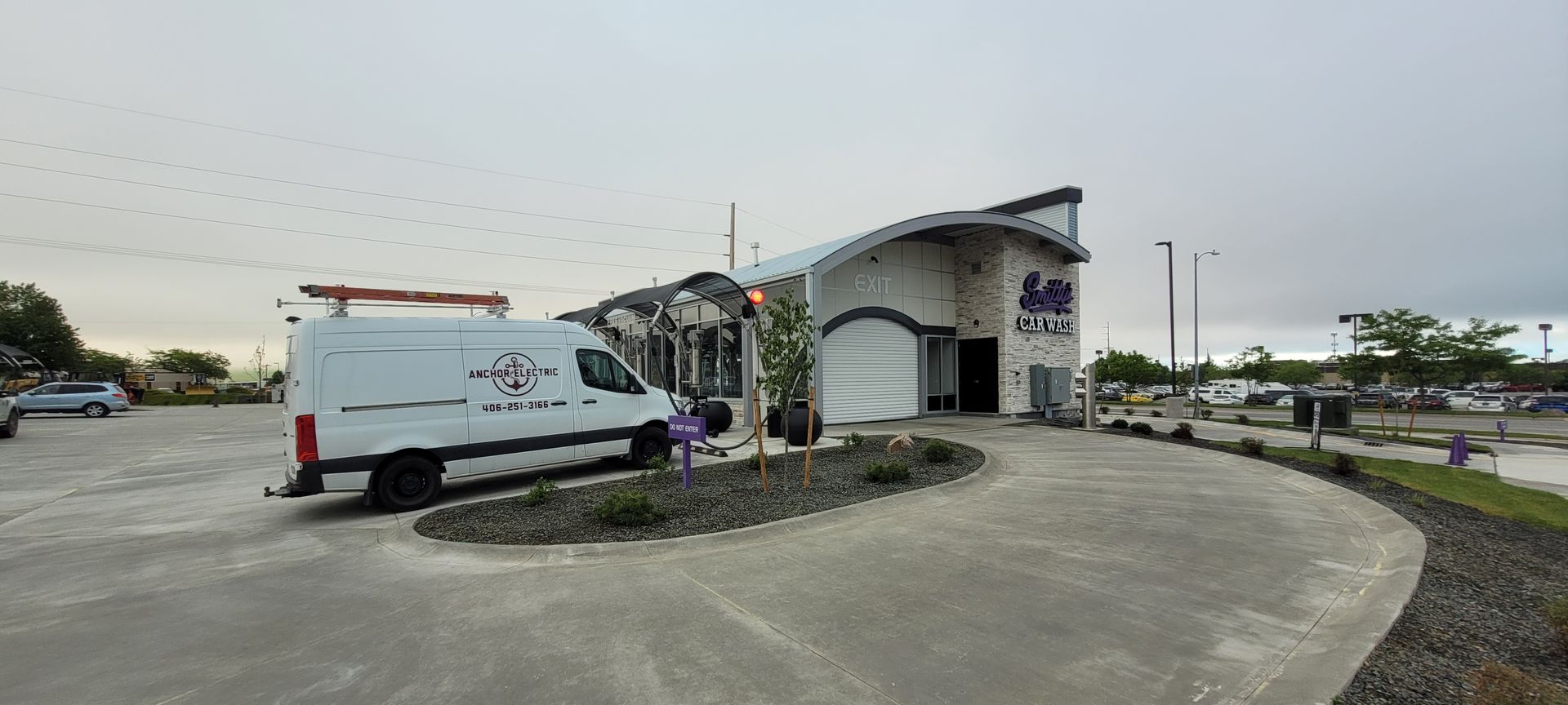 A white van parked in front of a modern building with a curved roof under an overcast sky.