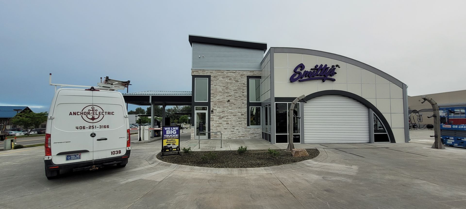 Exterior of a modern building with stone and metal accents; a white van is parked nearby.