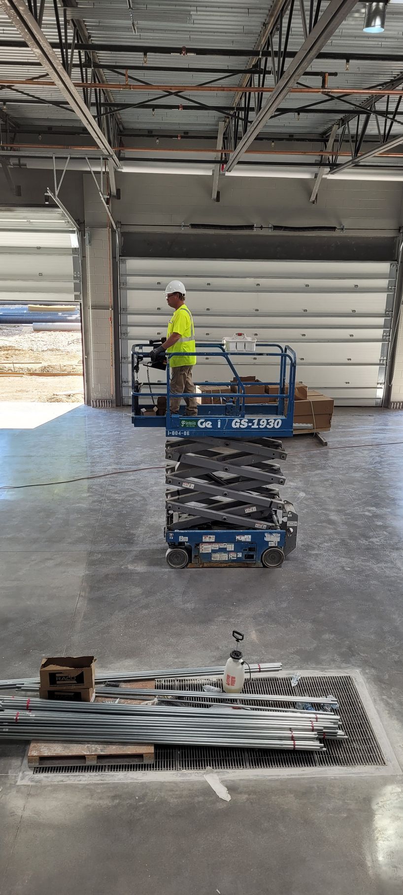 Construction worker in a lift, working near a garage door. Building interior, concrete floor, equipment.