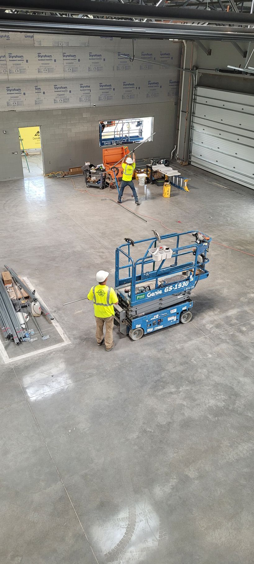 Construction workers operate equipment in a large, unfinished building.