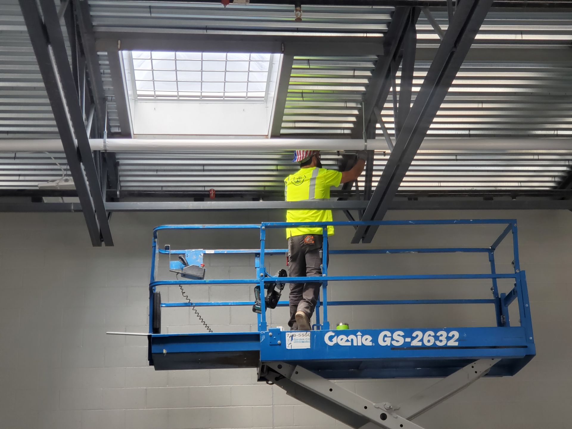 Construction worker on a scissor lift installs piping to a steel beam in a building.