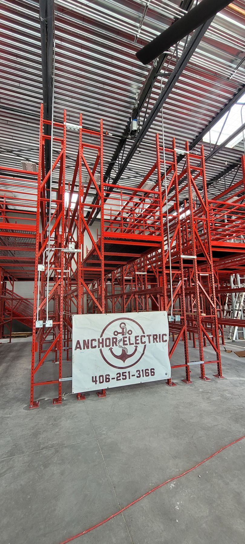 Red industrial scaffolding in a warehouse, with a sign for Anchor Secure.