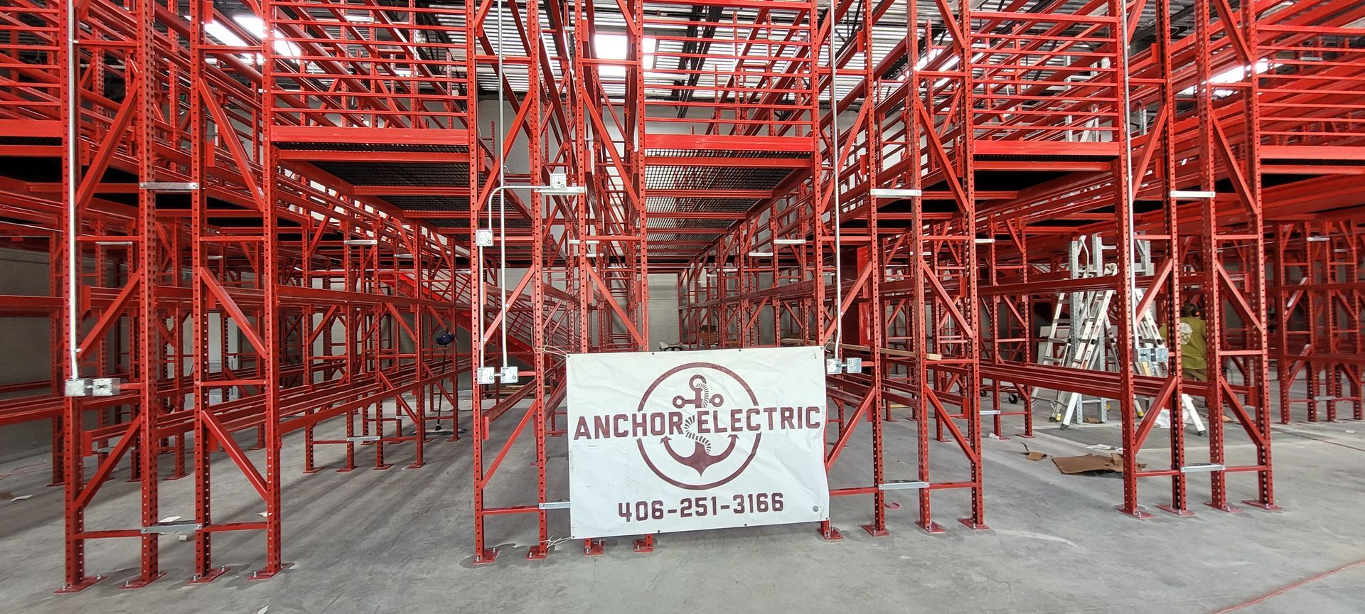 Red metal storage racks in a warehouse. Anchor Electric sign in the foreground.
