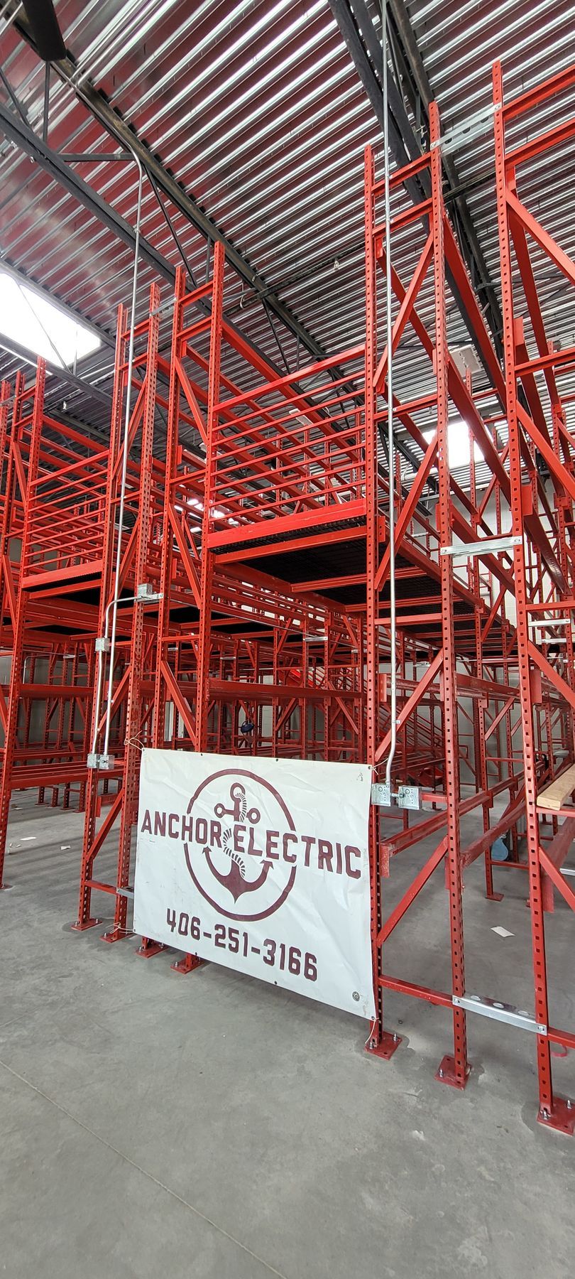 Red scaffolding structure in a warehouse; banner for Anchor Electric, phone number visible.