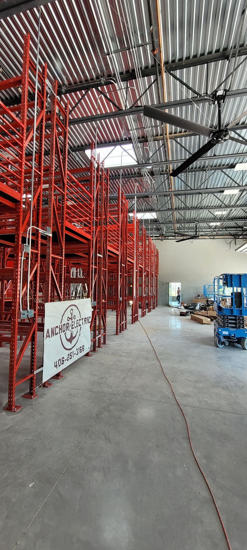 Inside of a warehouse with red shelving, a large fan, and a sign.