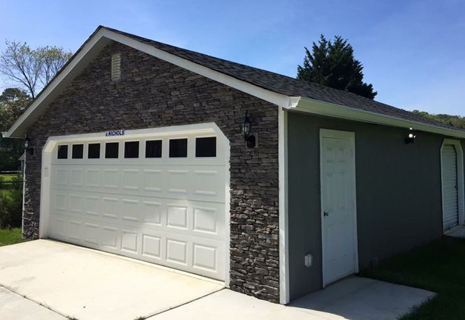 Garage with stone veneer, white garage door, and a green exterior. Concrete driveway.