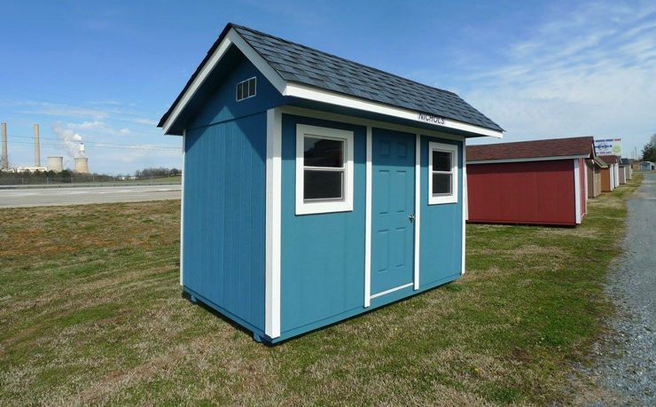 Blue shed with white trim and a shingled roof, on a grassy lot.