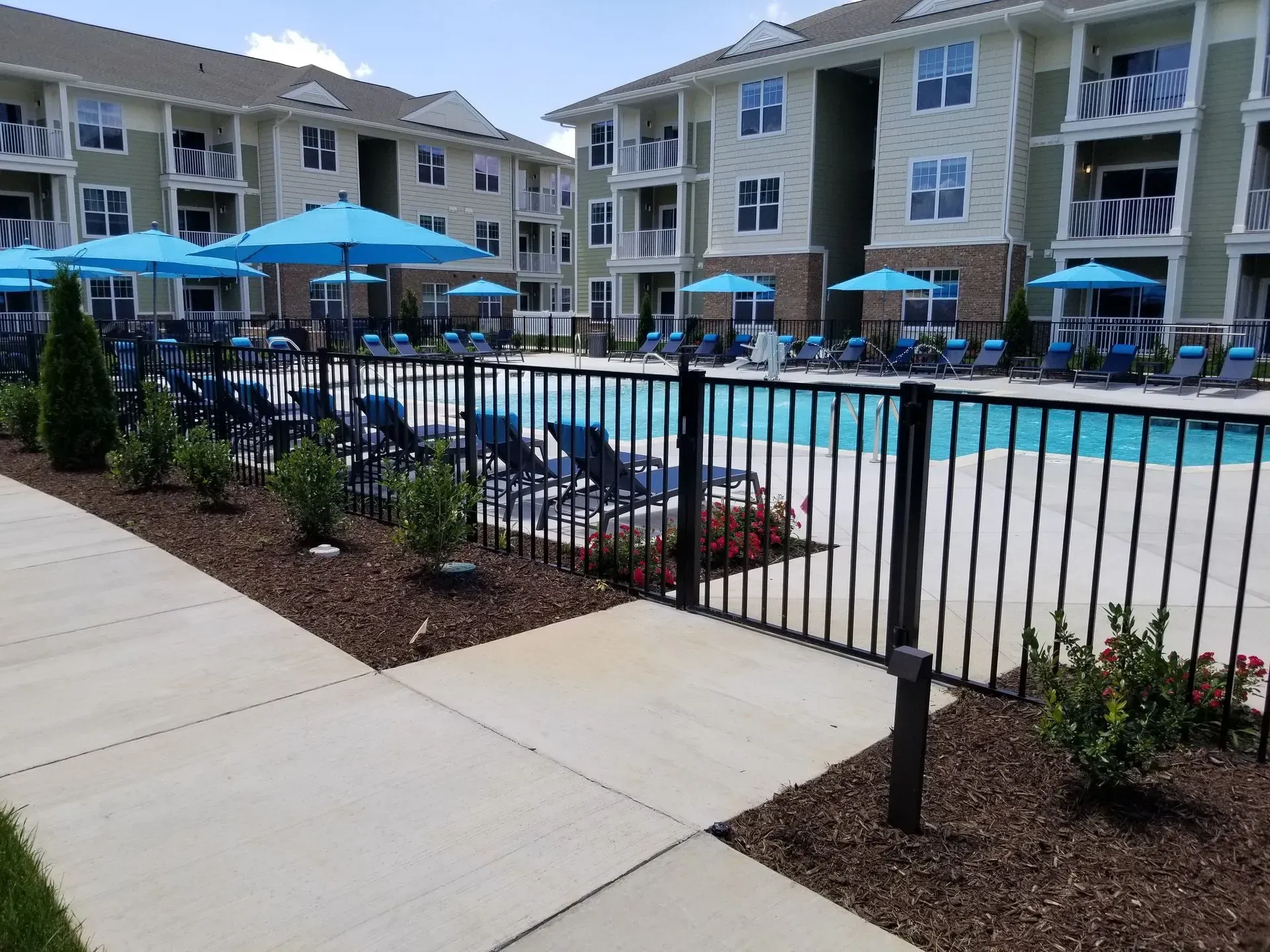 A fence surrounds a large swimming pool surrounded by chairs and umbrellas.