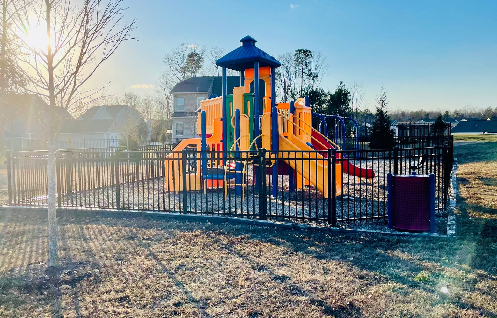 A playground with a fence around it and a house in the background.