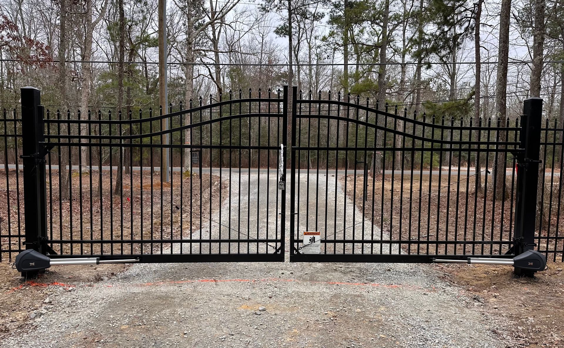 A black wrought iron gate is open to a gravel driveway.