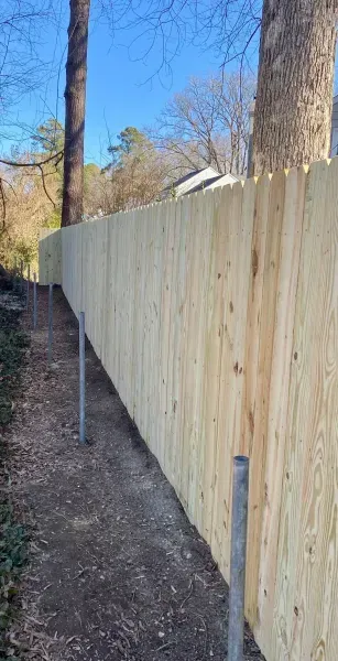 A wooden fence along a path with trees in the background.