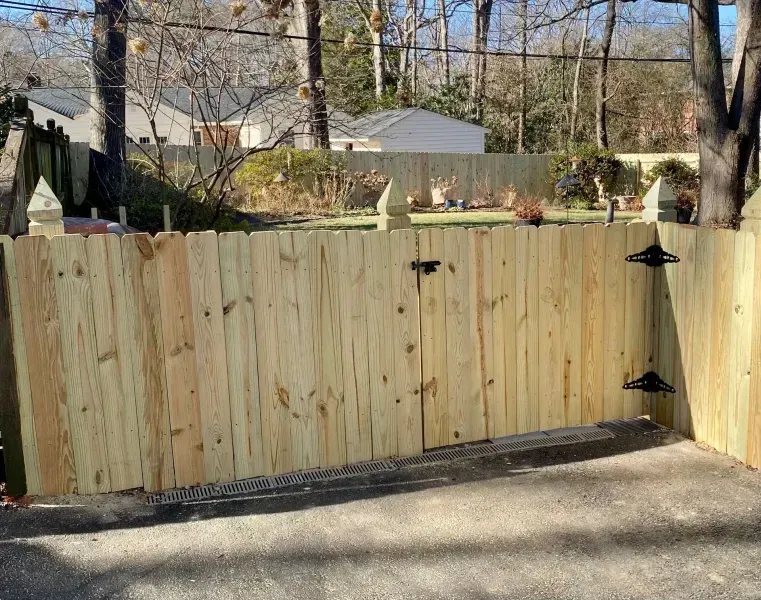 A wooden fence with a gate in the middle of a driveway.