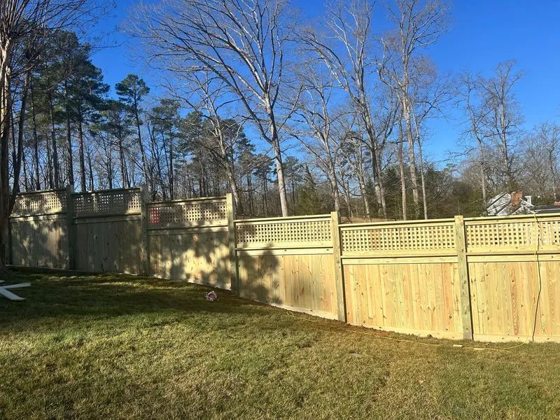 A wooden fence in a backyard with trees in the background.