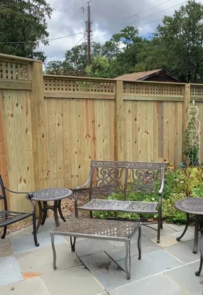 A wooden fence surrounds a patio with chairs , tables and a bench.