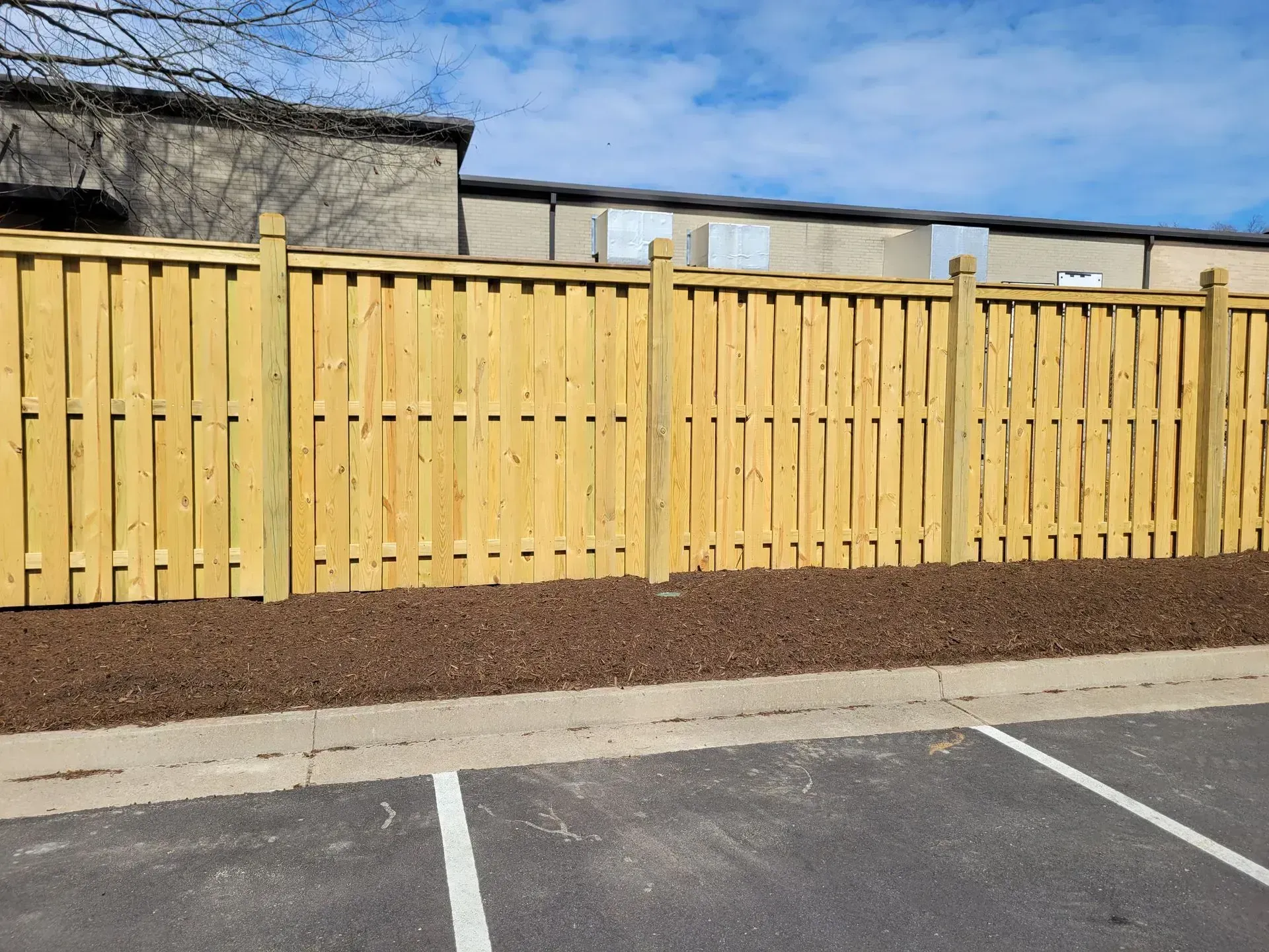 A wooden fence surrounds a parking lot with a building in the background.