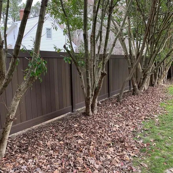 A wooden fence surrounded by trees and leaves in a yard.