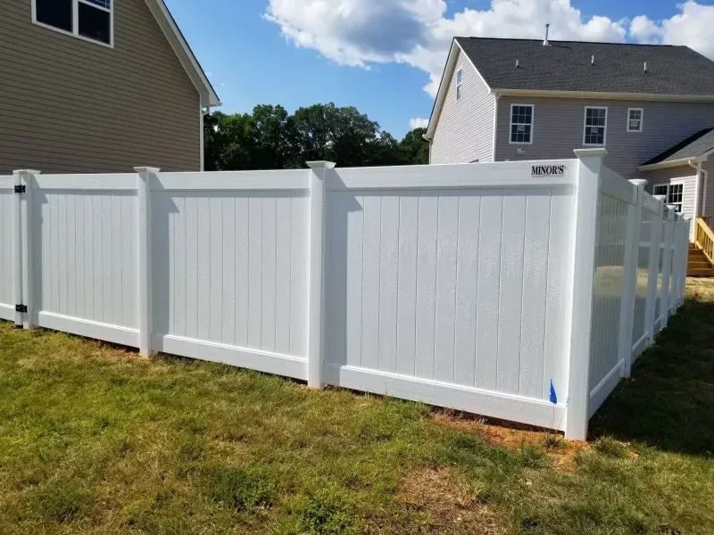 A white fence is sitting in the grass in front of a house.