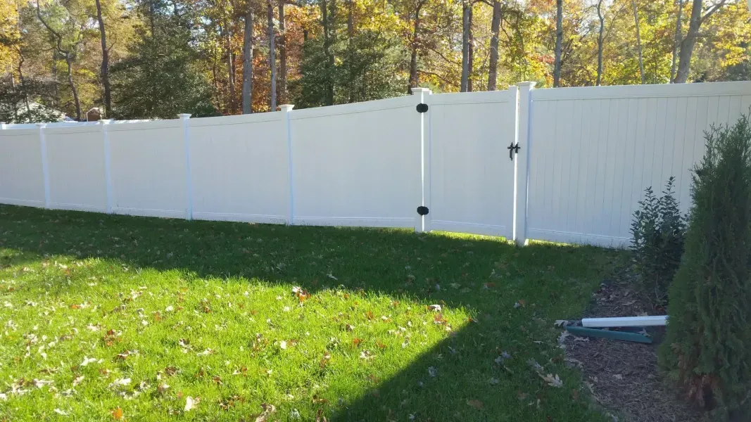 A white fence surrounds a lush green yard with trees in the background.