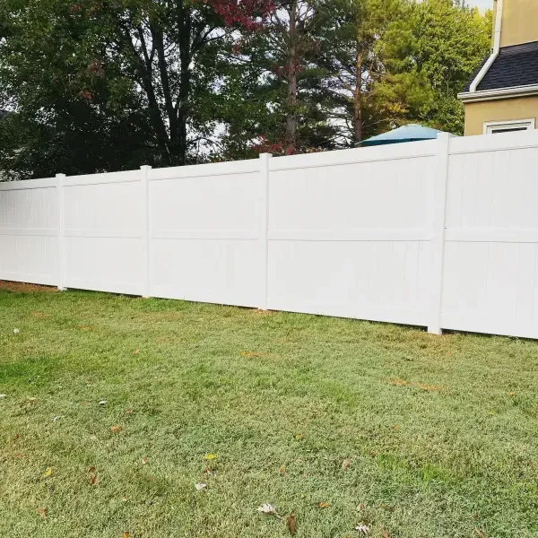 A white fence surrounds a lush green yard in front of a house.