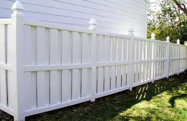 A white fence is sitting in the grass next to a white house.