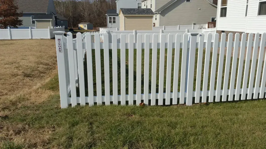 A white picket fence is sitting in the grass in front of a house.