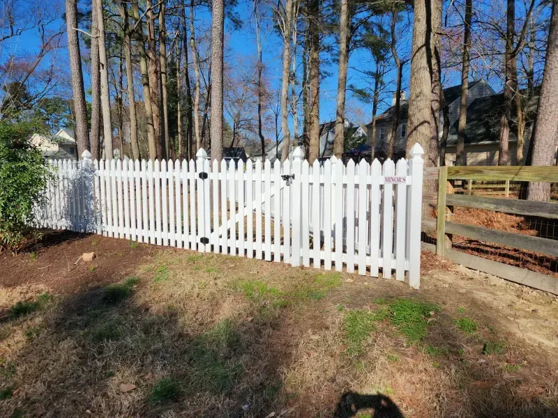 A white picket fence is surrounded by trees in a yard.