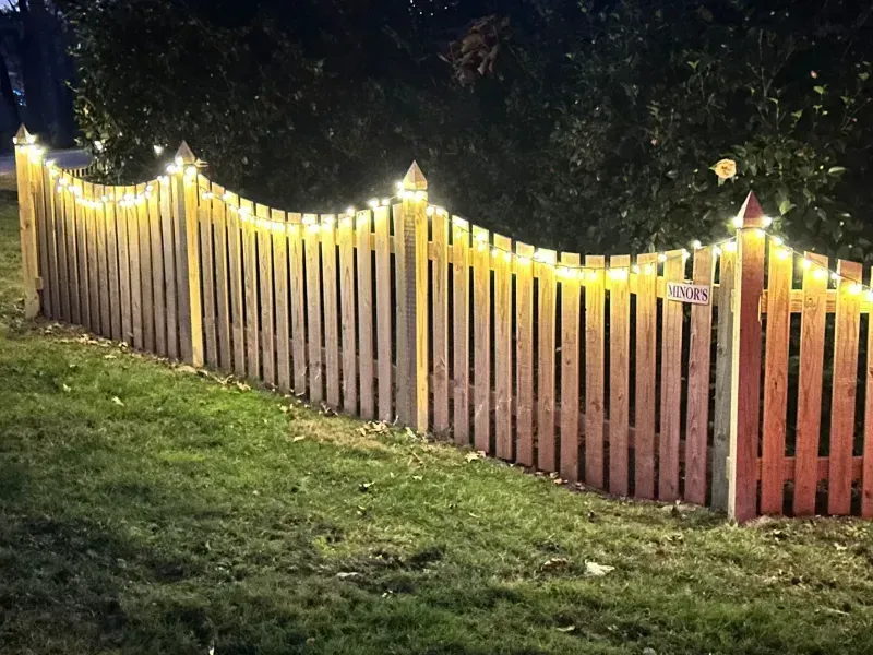 A wooden fence is decorated with christmas lights at night.