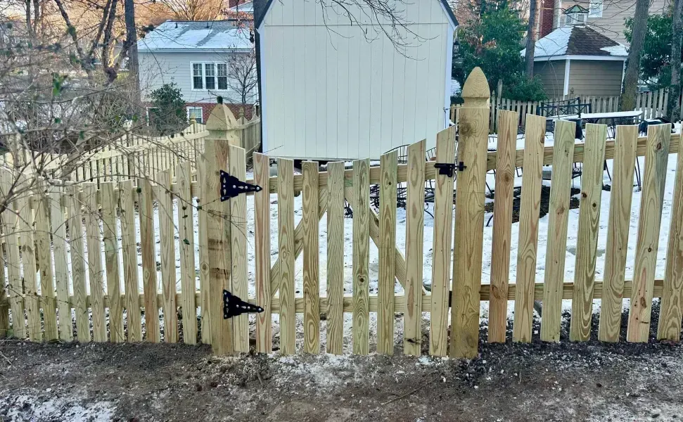 A wooden picket fence with a gate in front of a shed.