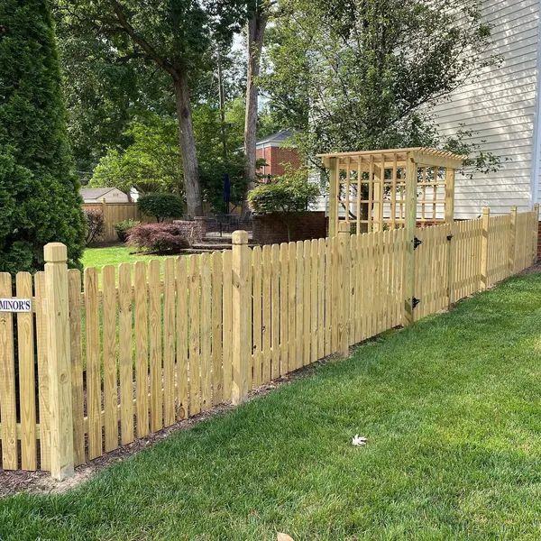 A wooden picket fence surrounds a lush green yard in front of a house.