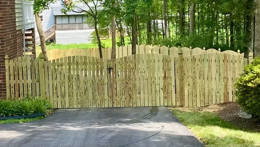A wooden fence surrounds a driveway leading to a house.