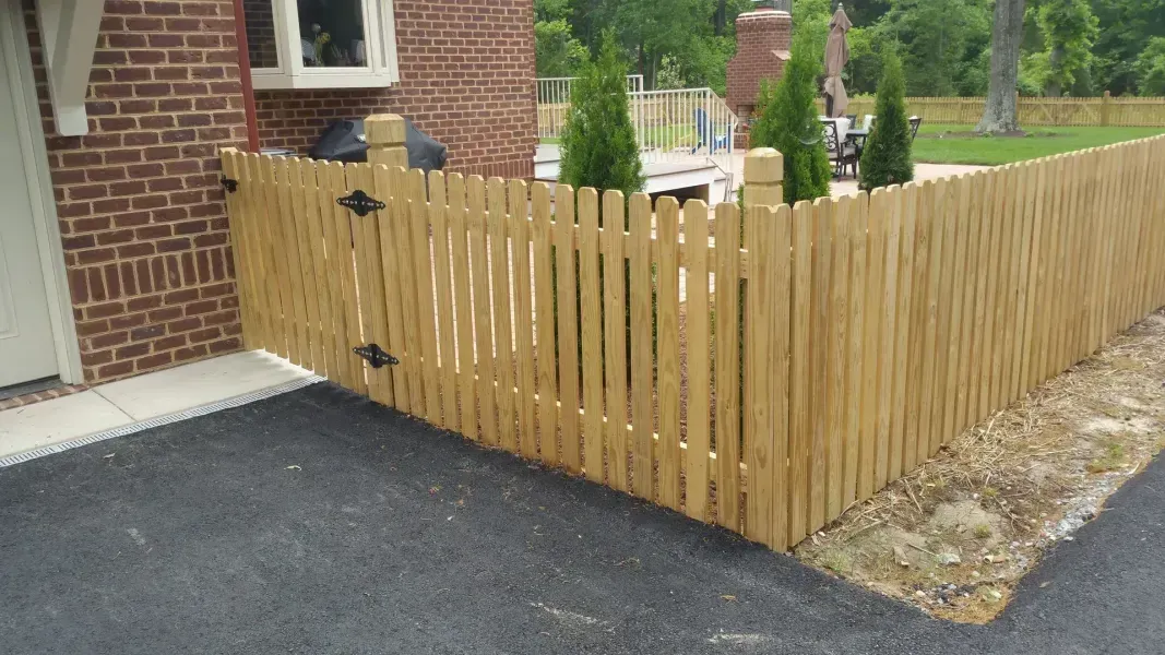 A wooden picket fence is in front of a brick house.