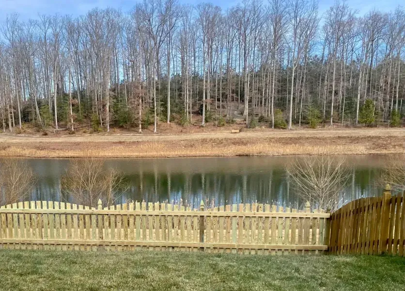 A wooden fence surrounds a lake with trees in the background.