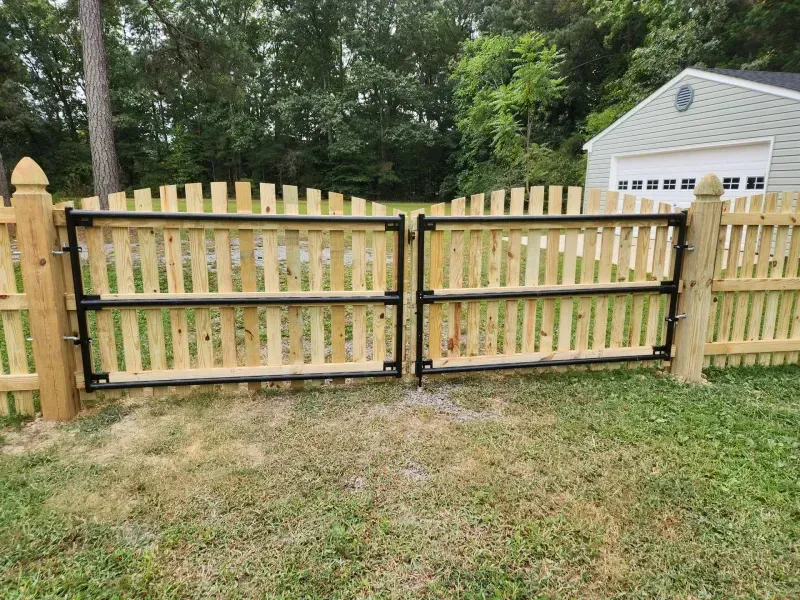 A wooden fence with a metal gate in front of a garage.