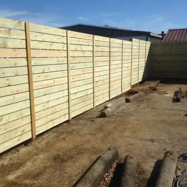 A wooden fence in a backyard with a house in the background