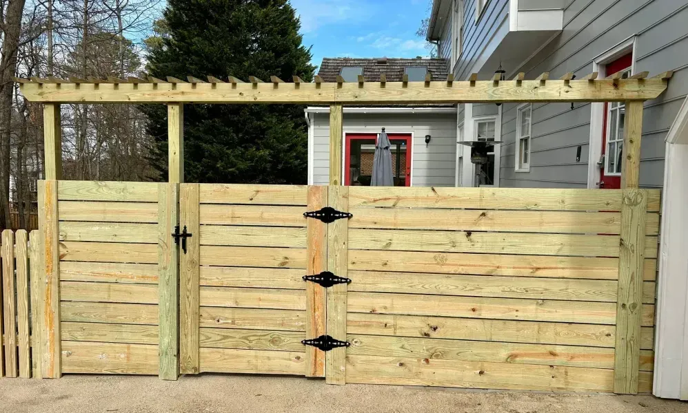 A wooden fence with a pergola attached to it is in front of a house.