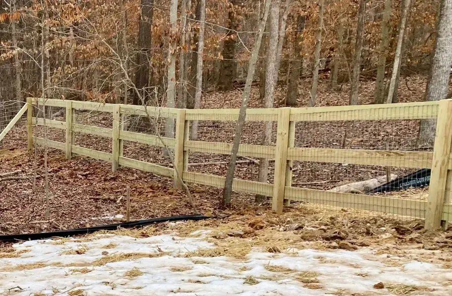 A wooden fence is surrounded by trees and snow in the woods.