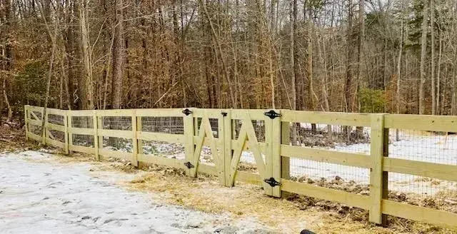A wooden fence with a gate in the middle of a snowy forest.