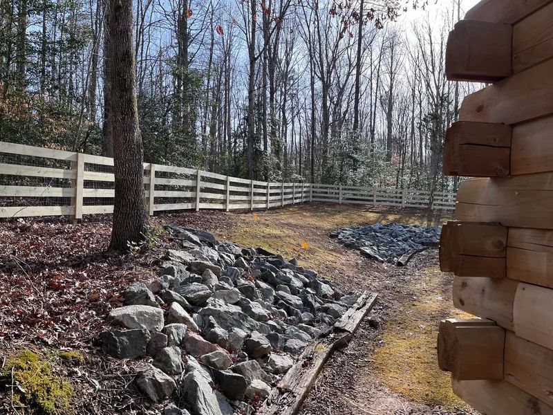 A log cabin is sitting next to a fence in the woods.
