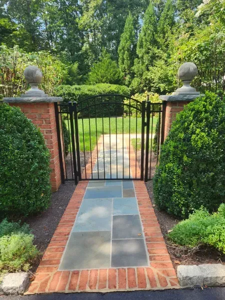 A brick walkway leading to a gate in a garden