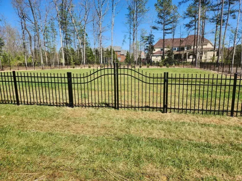 A black wrought iron fence surrounds a lush green field.