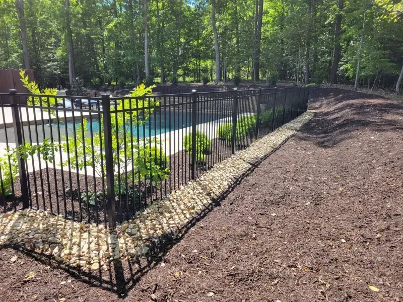 A black metal fence surrounds a swimming pool in a backyard.