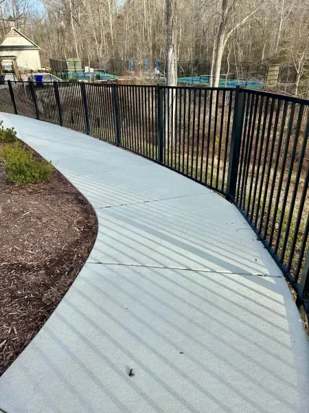 A concrete walkway with a metal fence along the side of it.
