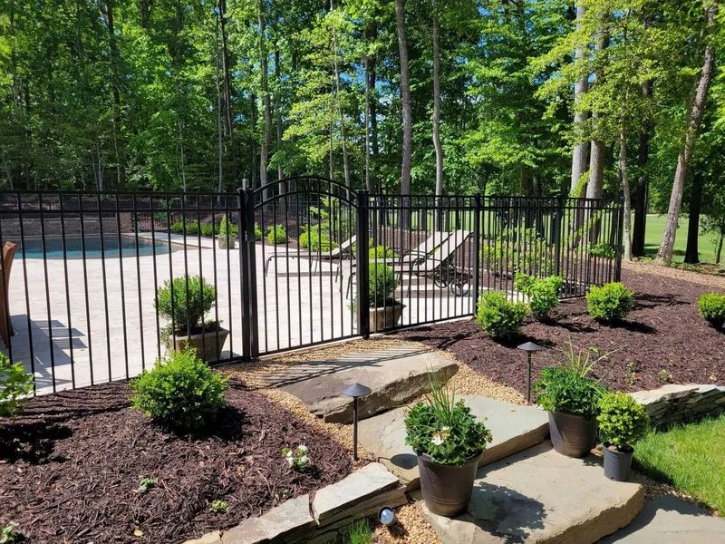 A black metal fence surrounds a swimming pool in a backyard.