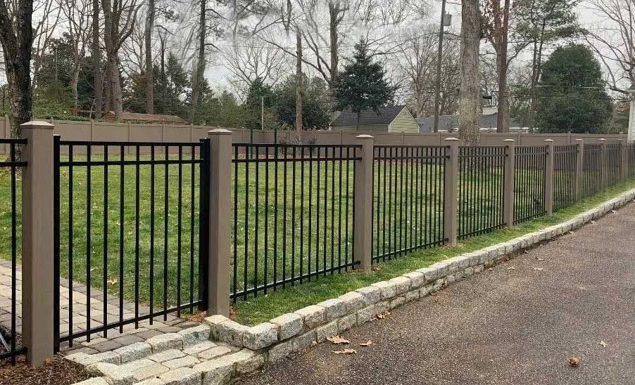 A metal fence surrounds a grassy field next to a road.