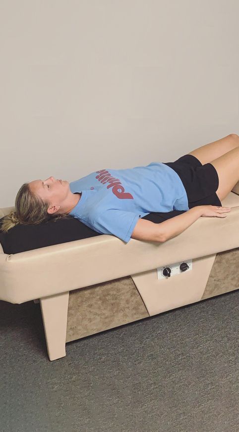 A woman in a blue shirt is laying on a massage table.