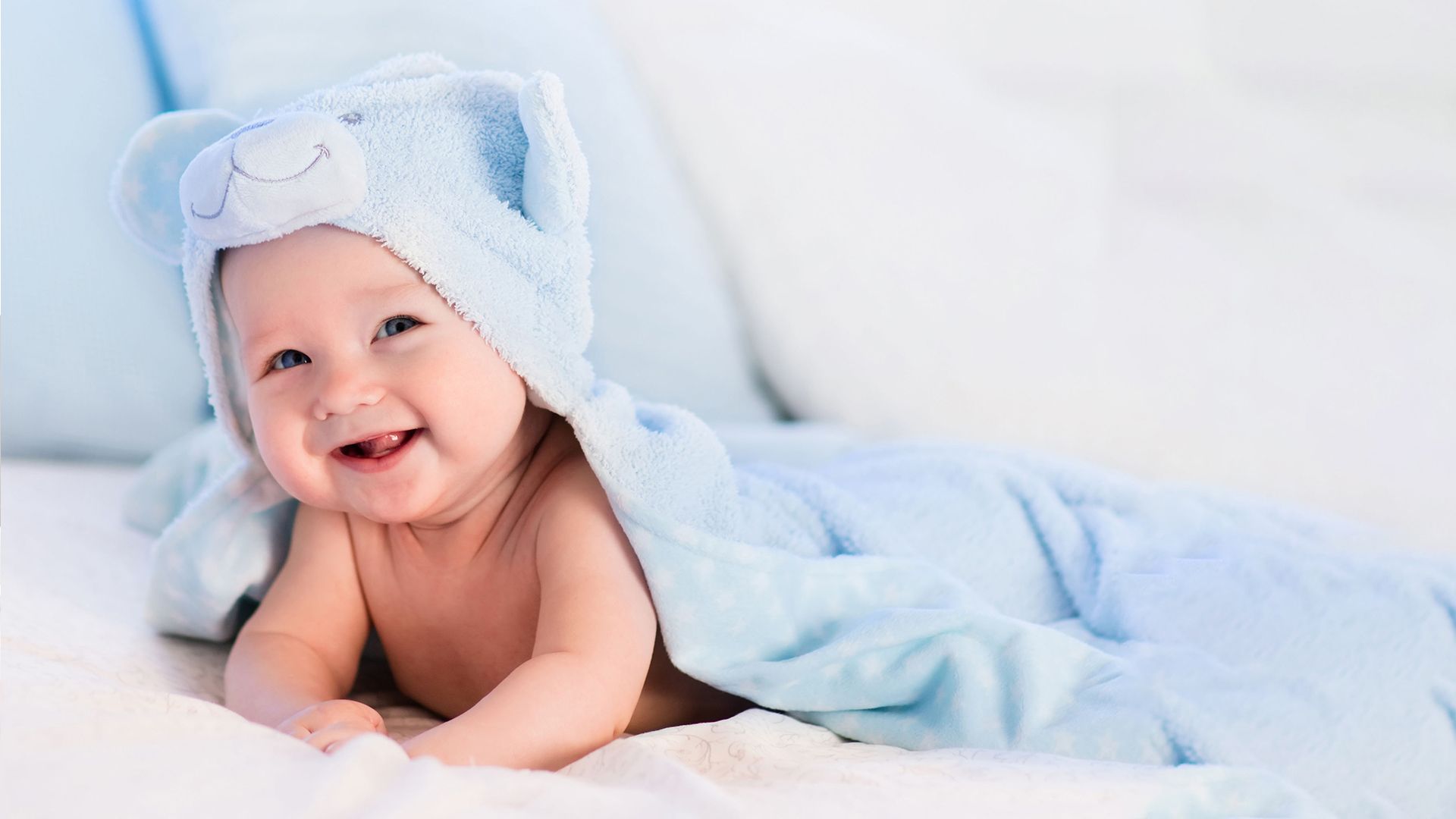 A baby is wrapped in a blue towel and smiling.