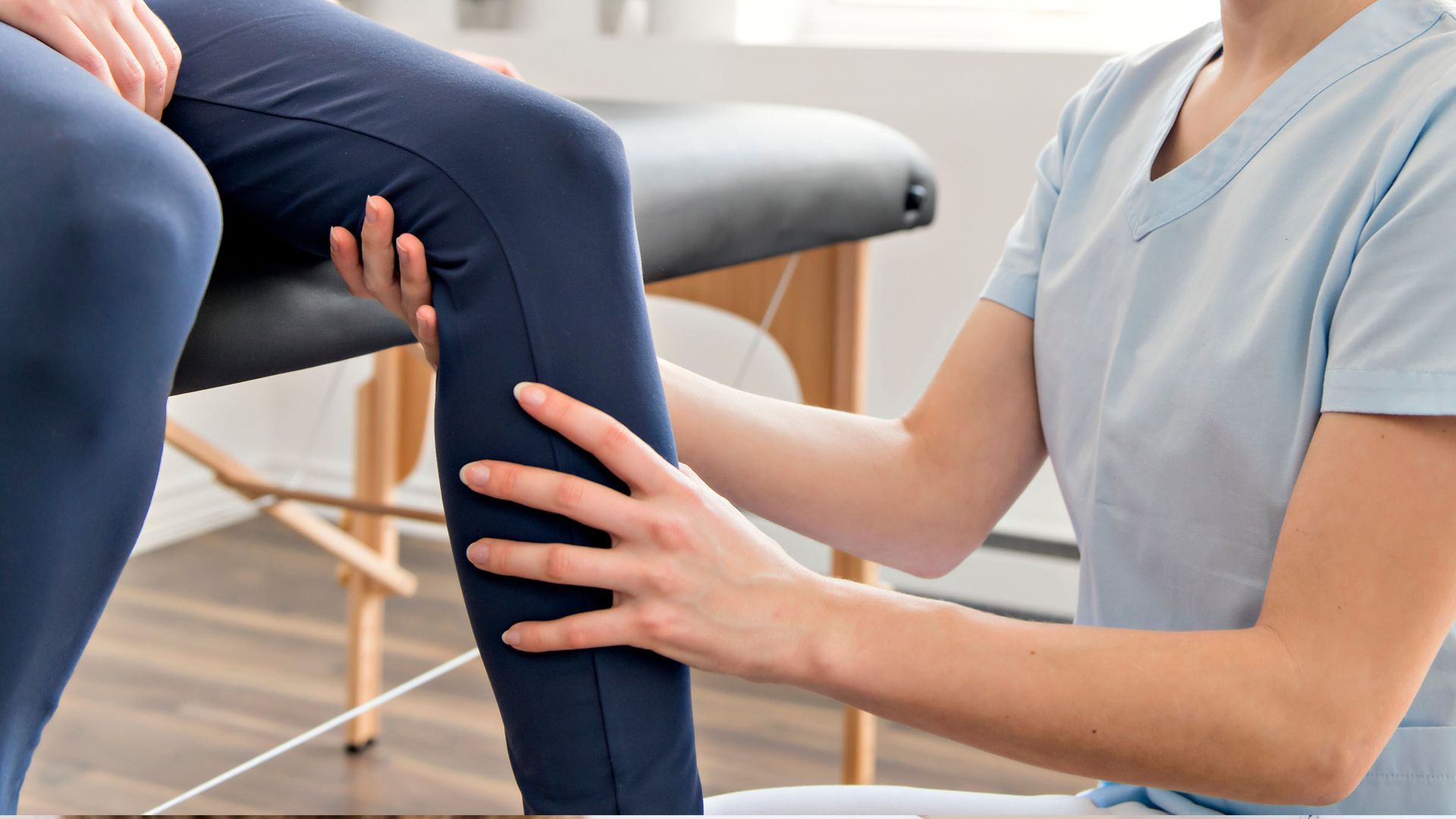 A chiropractor is examining a patient's leg while the patient sits in a chair.