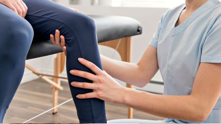 A chiropractor is examining a patient's leg while the patient sits in a chair.