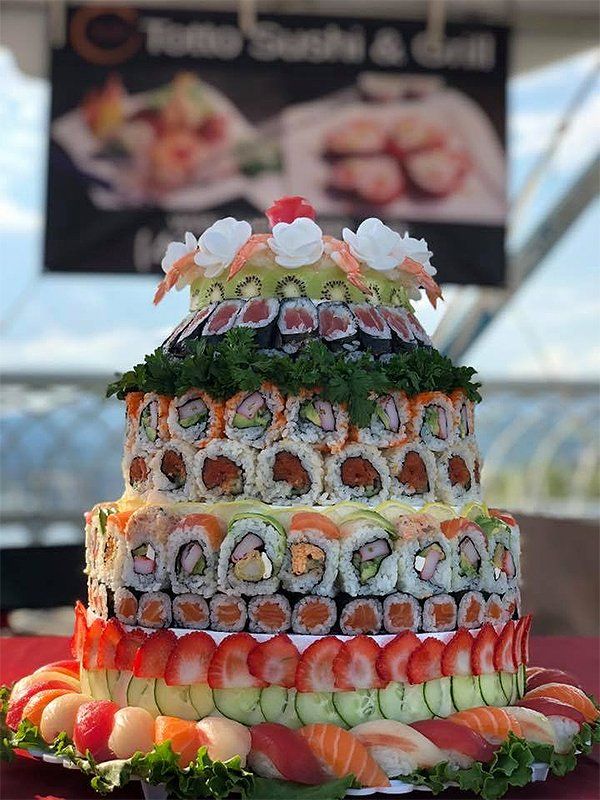 A cake made out of sushi and fruit is on a table.