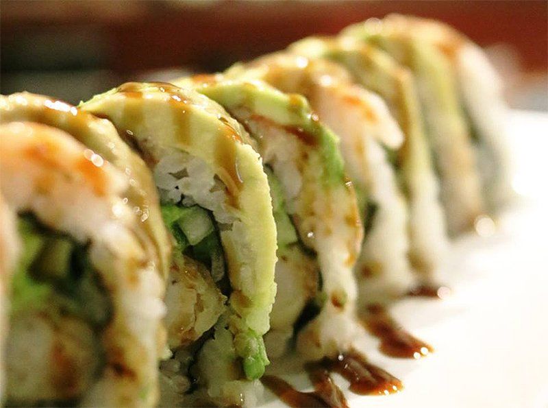 A row of sushi rolls with avocado and shrimp on a white plate